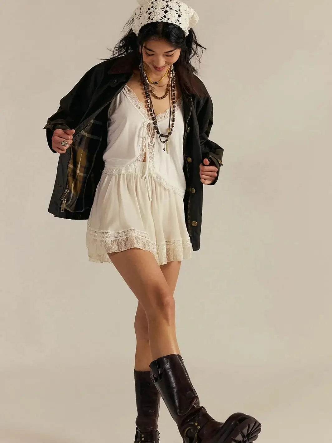 A model showcases the Free People Cori Waxed Jacket in Olive unzipped over a white lace-trimmed mini dress, revealing a classic plaid lining | Twentyseven Toronto