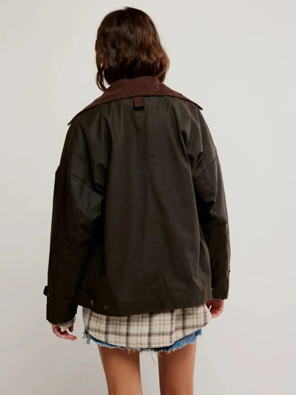 A  rear view highlights the clean panel lines and extended hemline of the Free People Cori Waxed Jacket in Olive layered over a longer plaid shirt. | Twentyseven Toronto