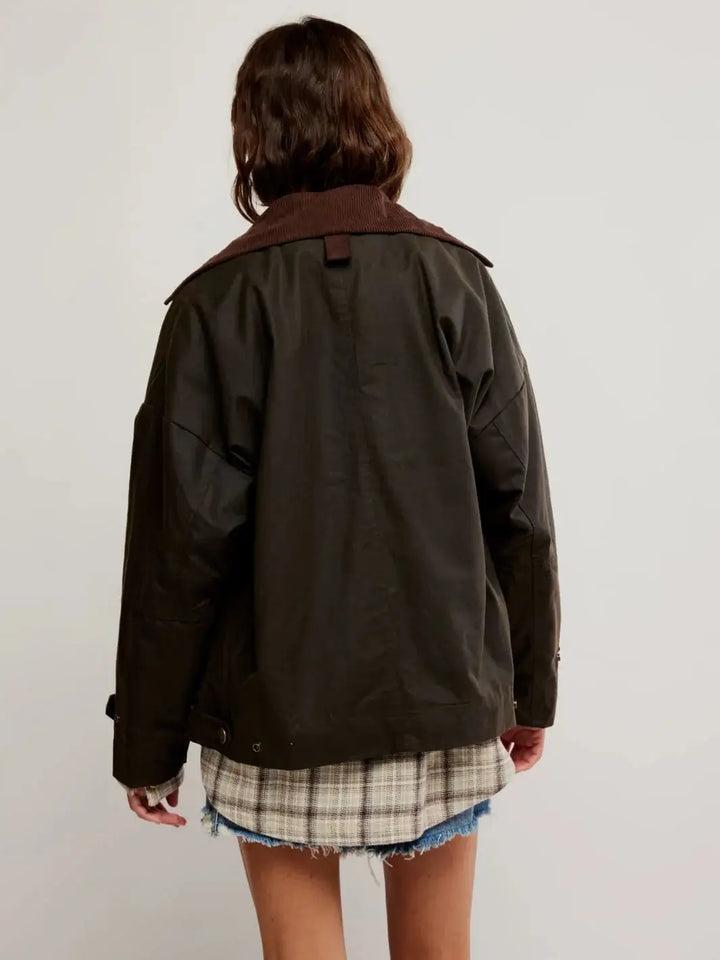 A  rear view highlights the clean panel lines and extended hemline of the Free People Cori Waxed Jacket in Olive layered over a longer plaid shirt. | Twentyseven Toronto