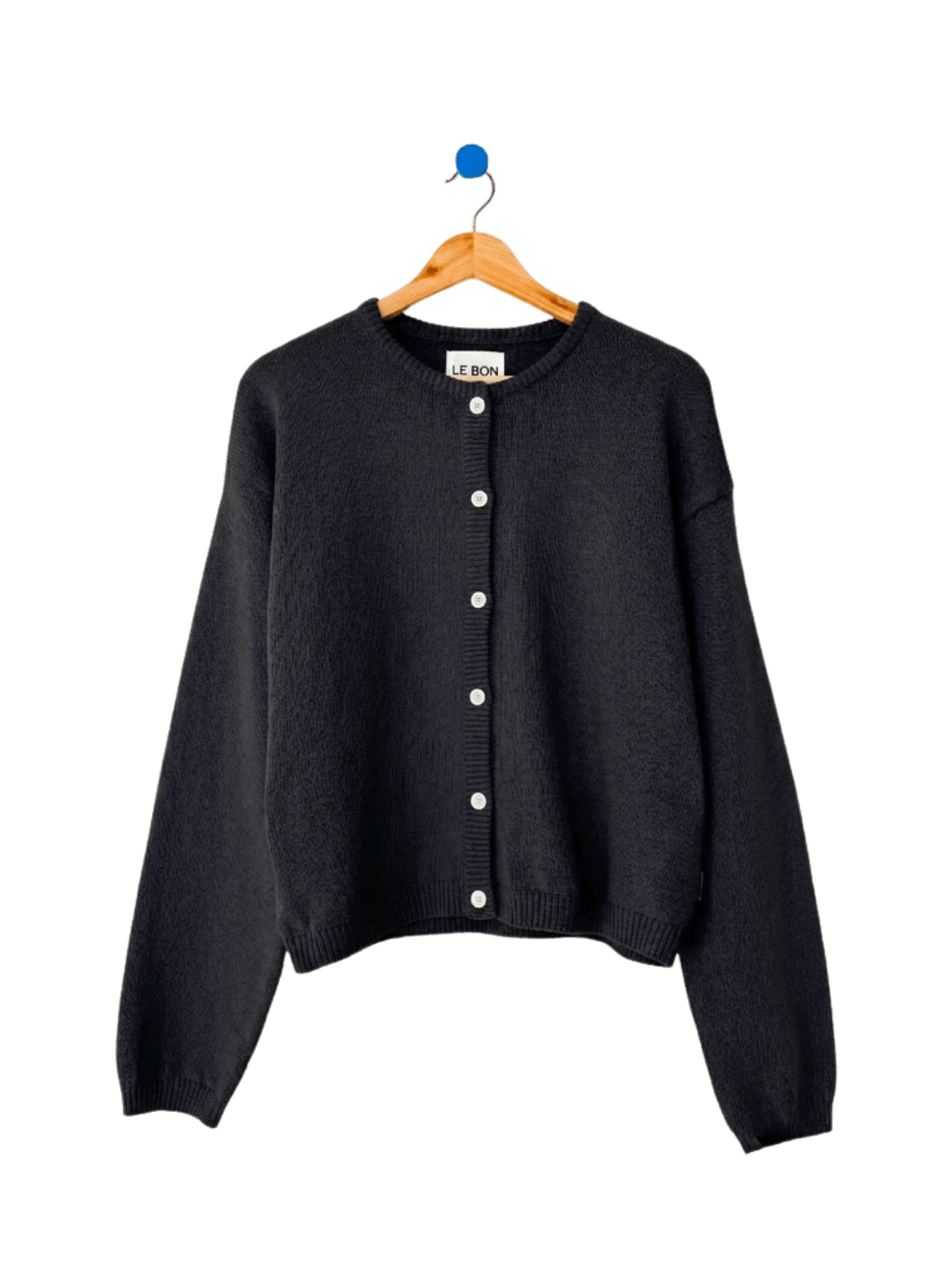 A flatlay image displays the classic button-down design and crew neckline of the Le Bon Shoppe Cotton Leila Cardigan - Black hanging on a wooden hanger | Twentyseven Toronto