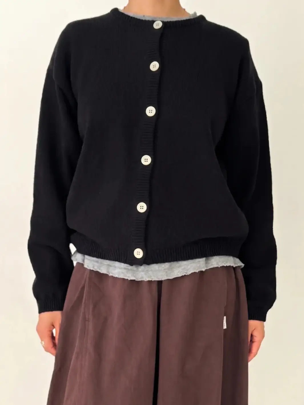 A person models the fully buttoned Le Bon Shoppe Cotton Leila Cardigan in Black layered over a grey shirt and brown pants | Twentyseven Toronto