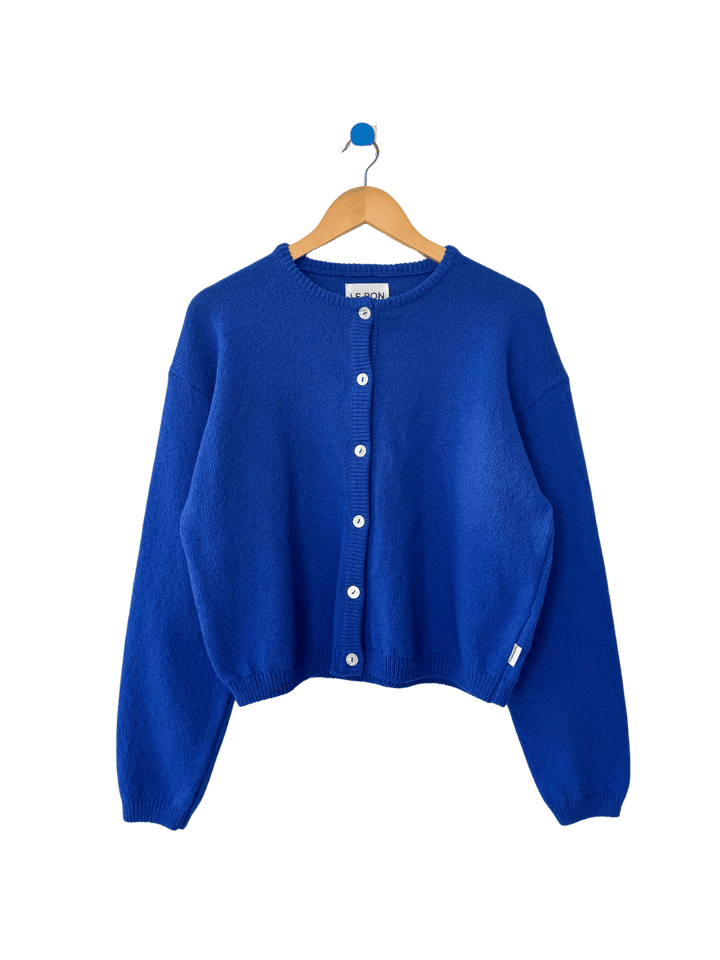 Blue 'Cotton Leila Cardigan' in 'Cobalt' from Le Bon Shoppe on a hanger against a transparent background | Twentyseven Toronto
