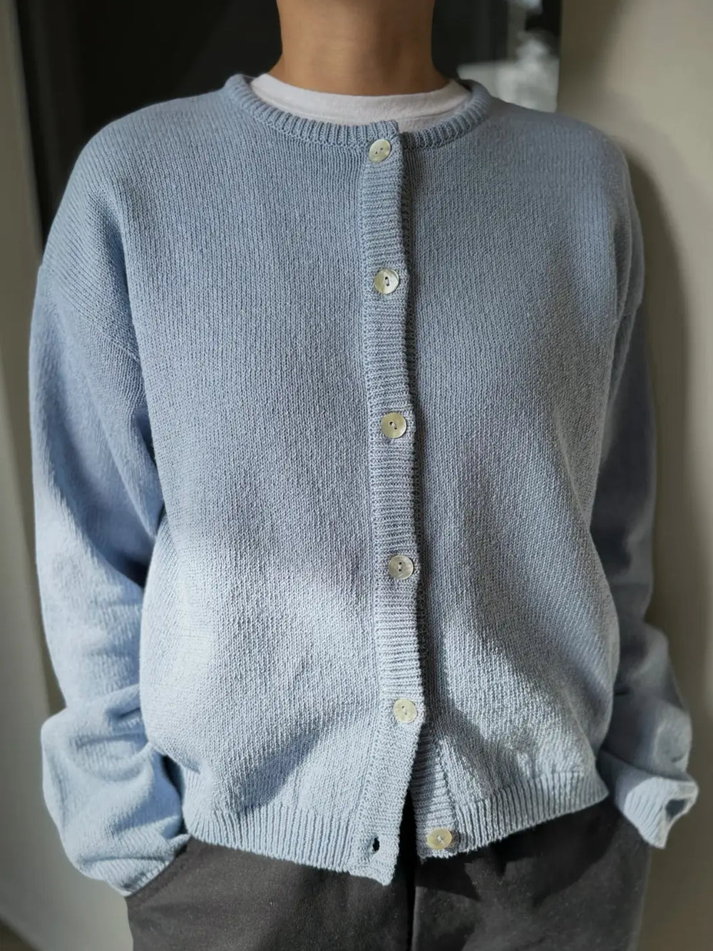 Person wearing a light blue 'Cotton Leila Cardigan' in 'Cornflower' with grey pants from Le Bon Shoppe in an indoor setting | Twentyseven Toronto