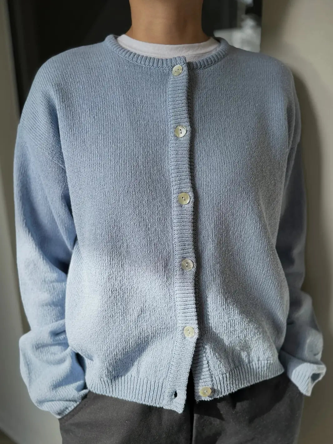 Person wearing a light blue 'Cotton Leila Cardigan' in 'Cornflower' with grey pants from Le Bon Shoppe in an indoor setting | Twentyseven Toronto