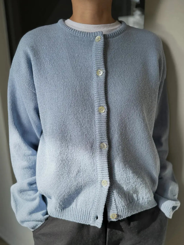 Person wearing a light blue 'Cotton Leila Cardigan' in 'Cornflower' with grey pants from Le Bon Shoppe in an indoor setting | Twentyseven Toronto