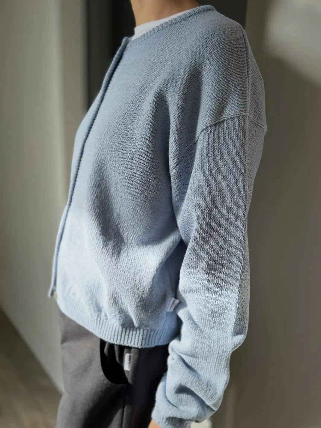 Side view of a person wearing a light blue 'Cotton Leila Cardigan' in 'Cornflower' with grey pants from Le Bon Shoppe in an indoor setting | Twentyseven Toronto