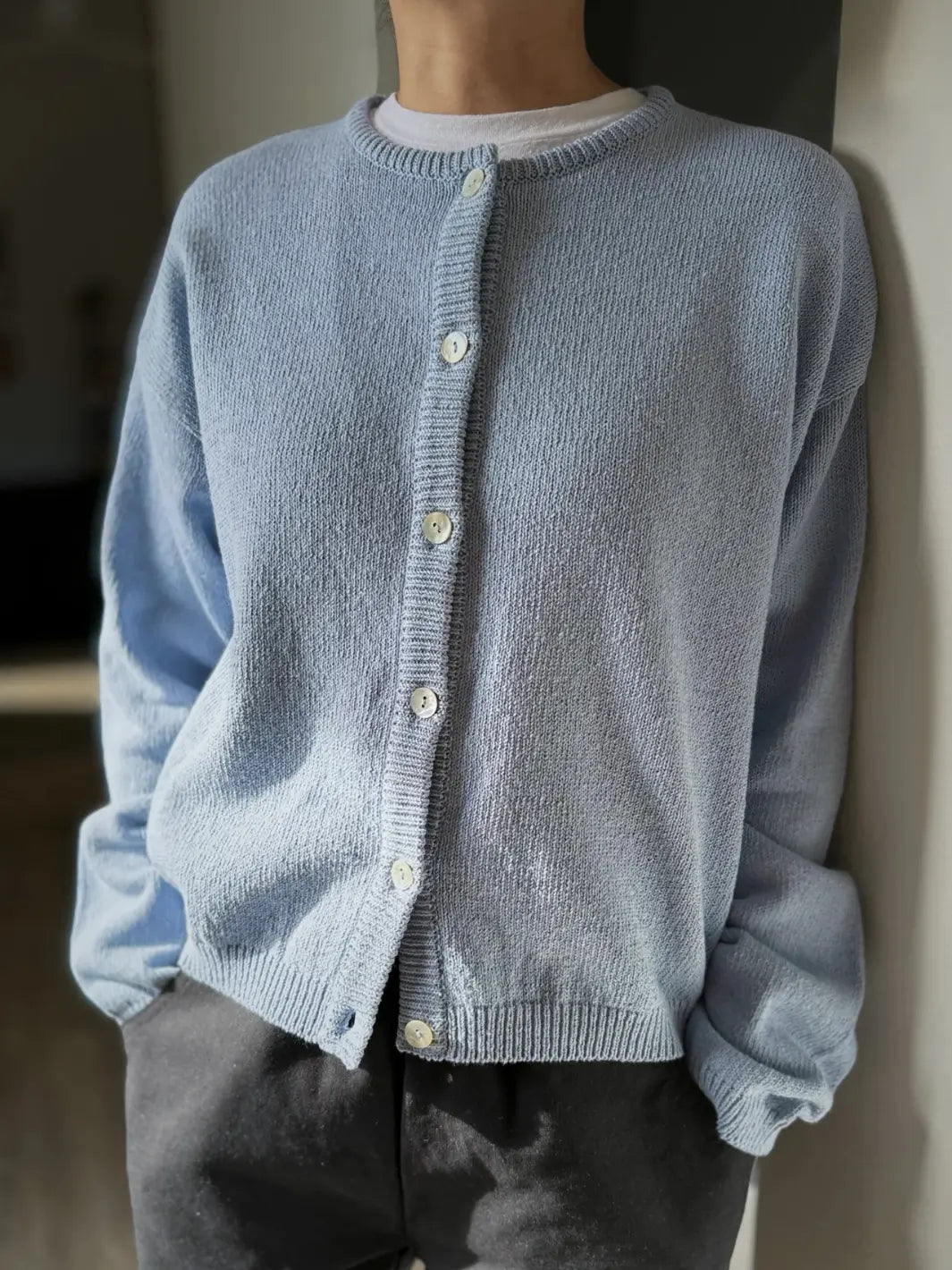 Person wearing a light blue 'Cotton Leila Cardigan' in 'Cornflower' with grey pants from Le Bon Shoppe in an indoor setting | Twentyseven Toronto
