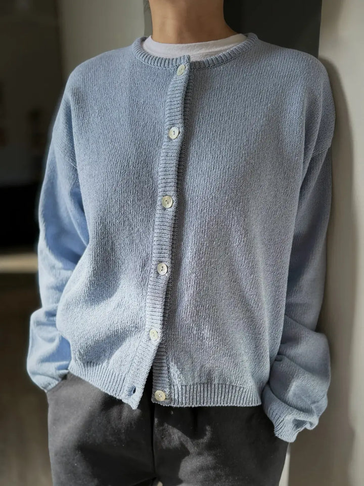 Person wearing a light blue 'Cotton Leila Cardigan' in 'Cornflower' with grey pants from Le Bon Shoppe in an indoor setting | Twentyseven Toronto