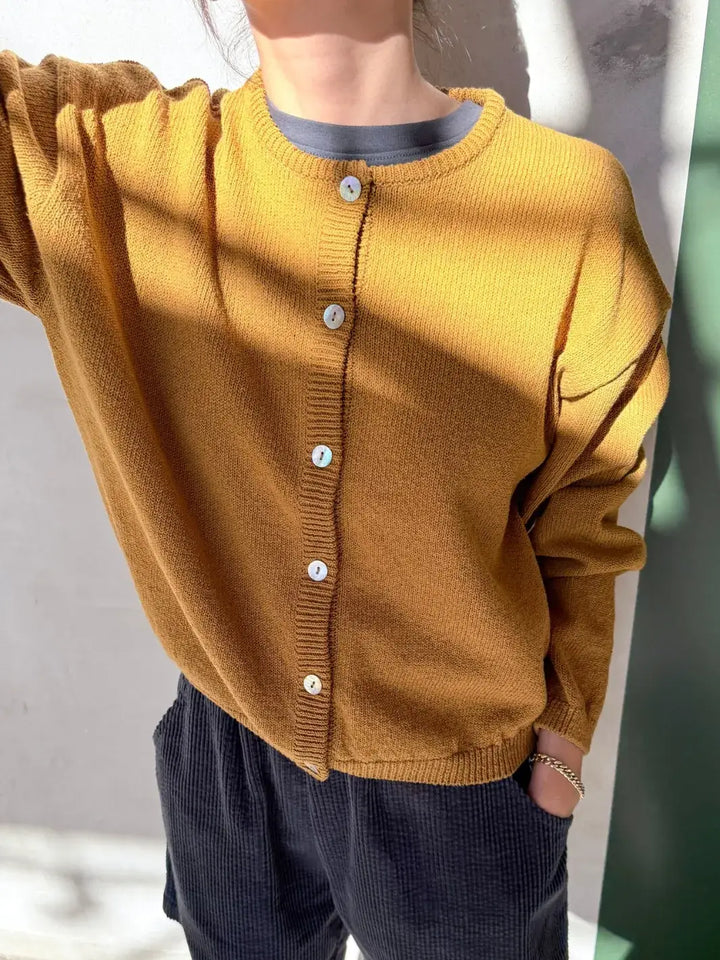 Person wearing a mustard yellow 'Cotton Leila Cardigan' in 'Dijon' with navy shorts from Le Bon Shoppe in an indoor setting | Twentyseven Toronto