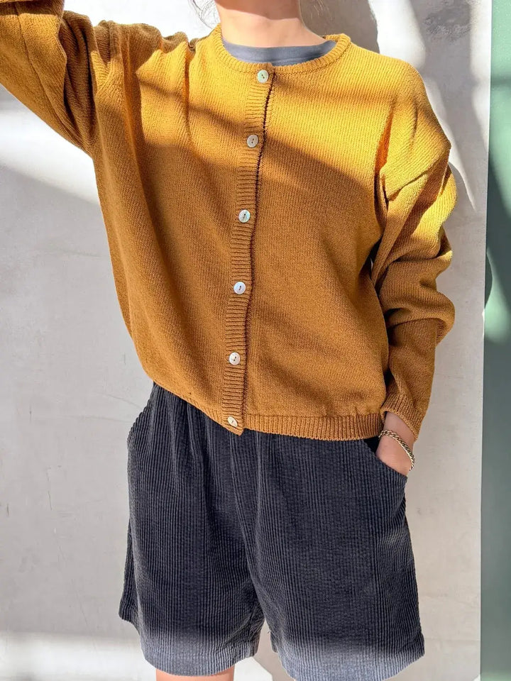 Person wearing a mustard yellow 'Cotton Leila Cardigan' in 'Dijon' with navy shorts from Le Bon Shoppe in an indoor setting | Twentyseven Toronto