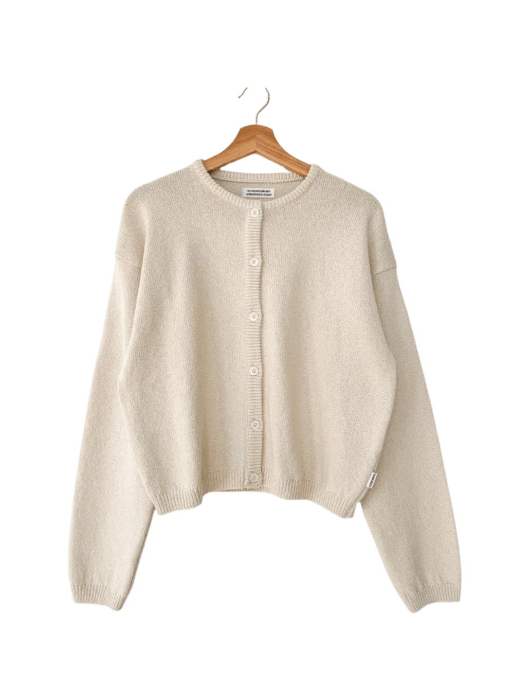 A flat lay product image showcases the clean crewneck design and button-down closure of the Le Bon Shoppe Cotton Leila Cardigan - Naturel hanging on a wooden hanger | Twentyseven Toronto