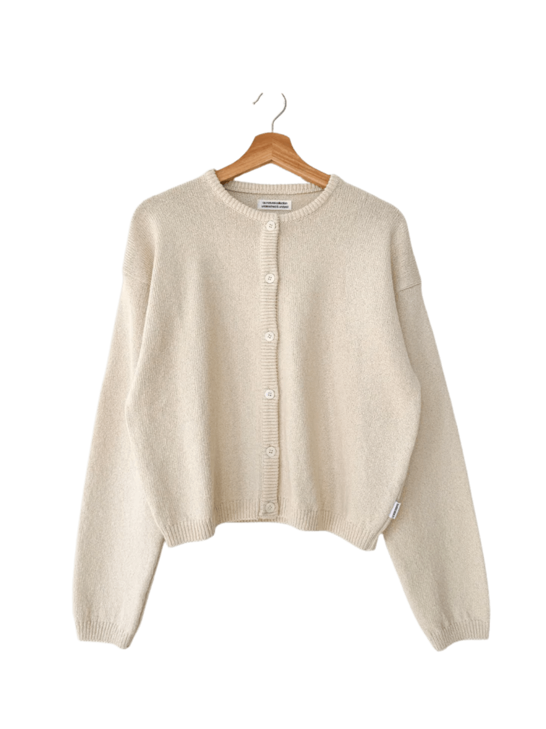 A flat lay product image showcases the clean crewneck design and button-down closure of the Le Bon Shoppe Cotton Leila Cardigan - Naturel hanging on a wooden hanger | Twentyseven Toronto