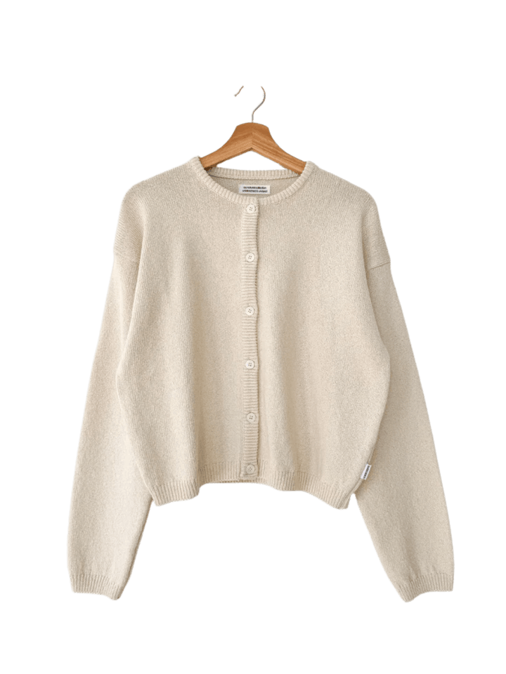 A flat lay product image showcases the clean crewneck design and button-down closure of the Le Bon Shoppe Cotton Leila Cardigan - Naturel hanging on a wooden hanger | Twentyseven Toronto