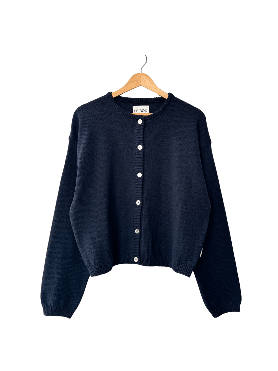 Dark blue 'Cotton Leila Cardigan' in 'Navy' from Le Bon Shoppe on a wooden hanger on transparent background | Twentyseven Toronto