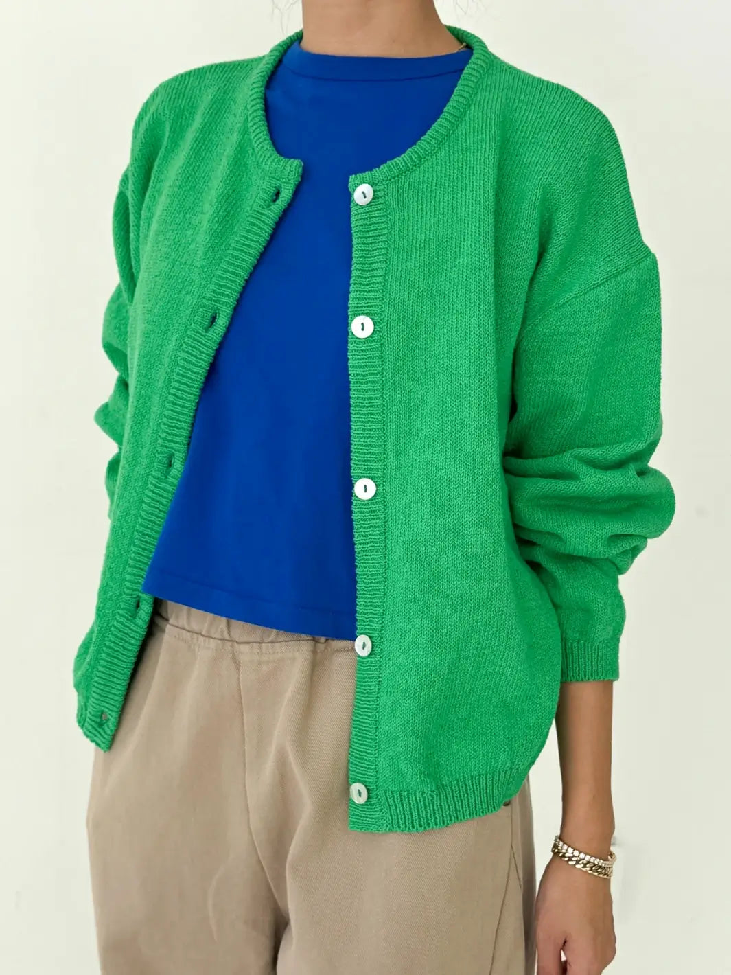 Person wearing a green 'Cotton Leila Cardigan' in 'Spring Green' over a blue shirt with beige pants from Le Bon Shoppe on a white background | Twentyseven Toronto