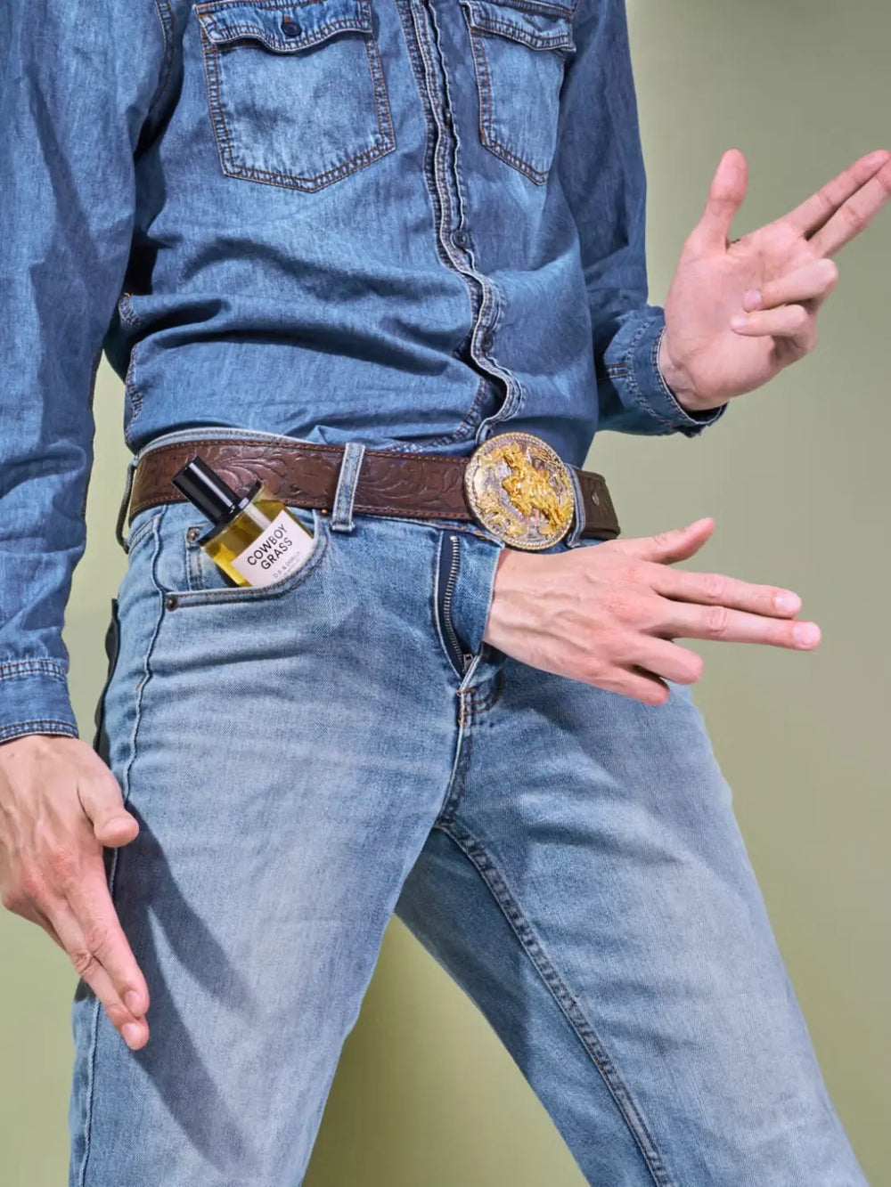 Person in a blue denim clothing with 3 hands and 50ml perfume bottle labeled 'Cowboy Grass' by D.S. & Durga on a green background | Twentyseven Toronto
