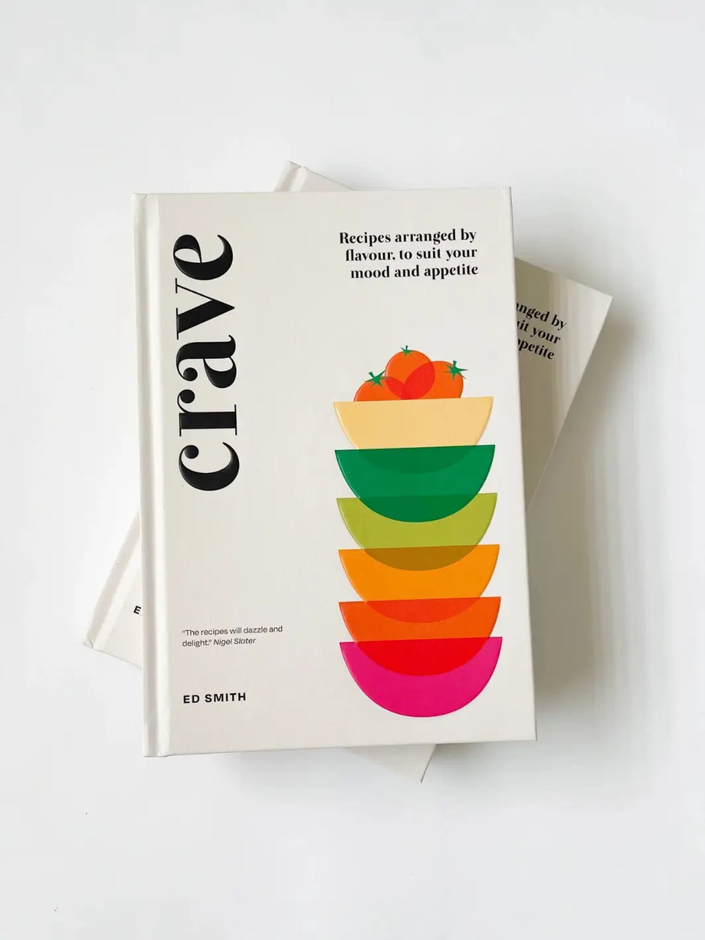 Copies of Crave: Recipes Arranged by Flavour, to Suit Your Mood and Appetite by Ed Smith rests on top of another copy of the book, highlighting the minimalist cover design and its stack of vibrant, multicolored bowls | Twentyseven Toronto