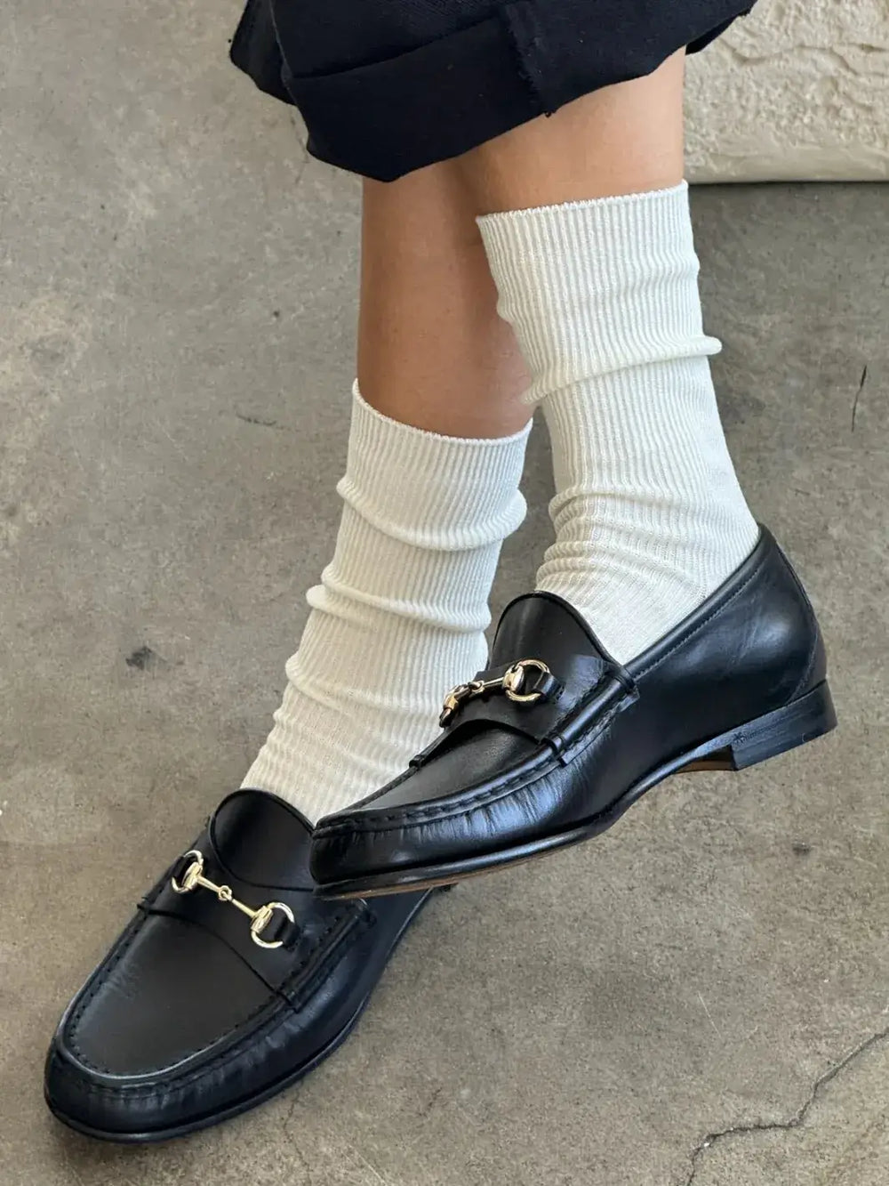 Black loafers with gold buckles worn with white 'Crisp Step Socks' from Le Bon Shoppe on a concrete floor | Twentyseven Toronto