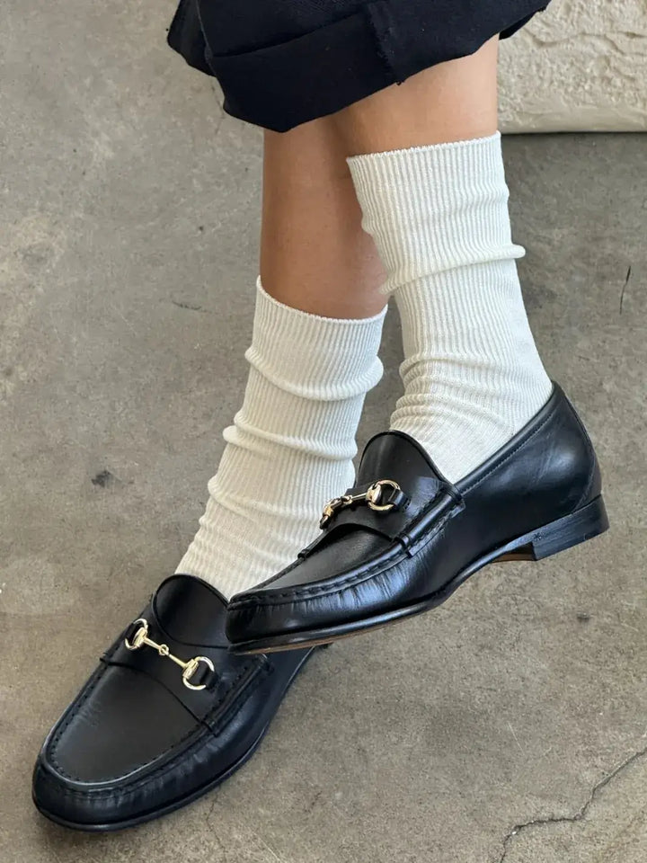 Black loafers with gold buckles worn with white 'Crisp Step Socks' from Le Bon Shoppe on a concrete floor | Twentyseven Toronto