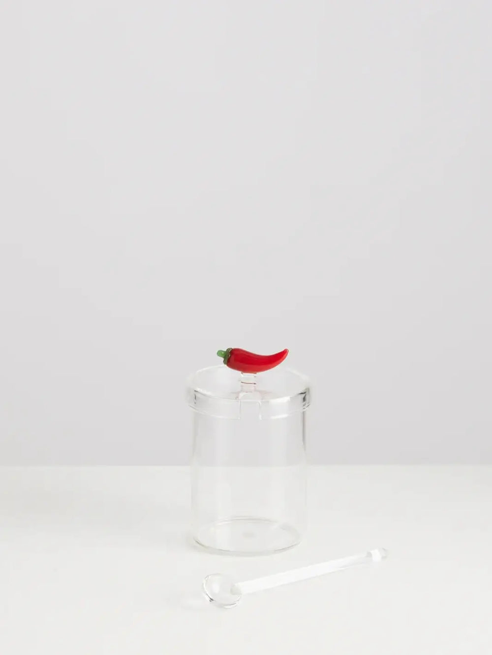 Clear crispy chili oil jar from Maison Balzac with a spoon, and a decorative red pepper design on a white background | Twentyseven Toronto