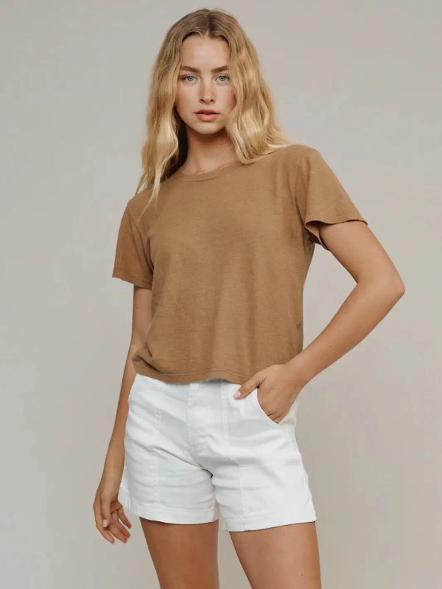 A model poses from the waist up to highlight the crew neckline, short sleeves, and relaxed fit of the Jungmaven Cropped Lorel Tee - Coyote styled with white shorts | Twentyseven Toronto