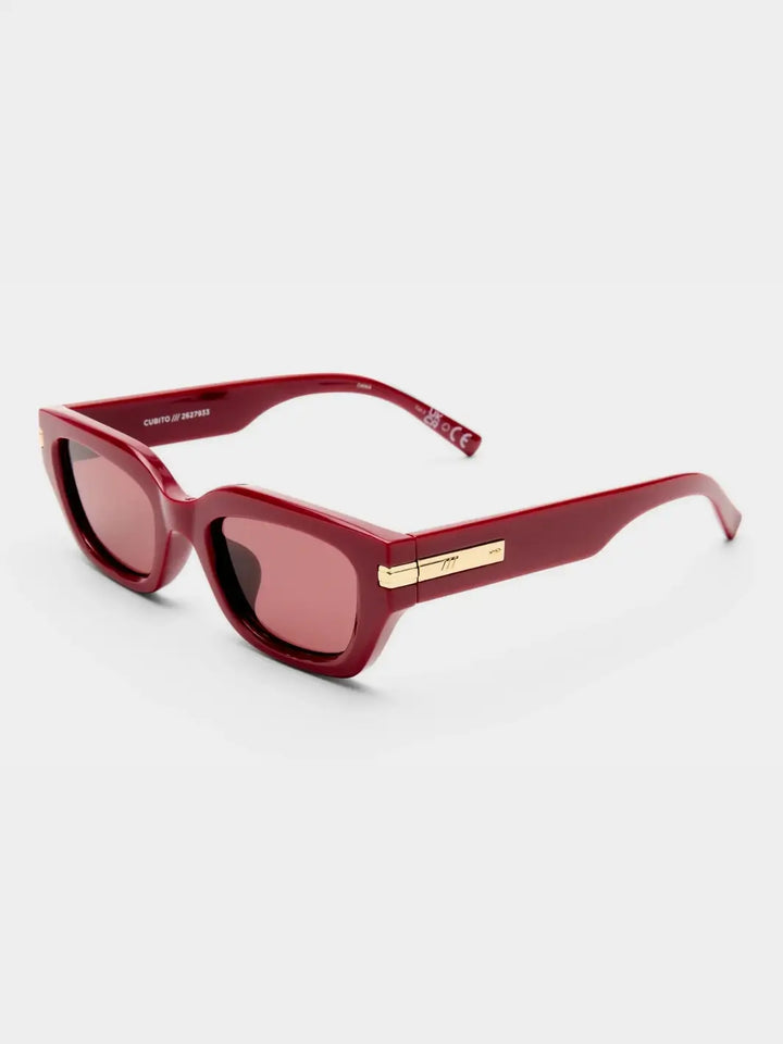 A three-quarter studio product shot of the Le Specs Cubito + Burgundy sunglasses showing their dark red frame, pink-tinted lenses, and gold temple accents | Twentyseven Toronto