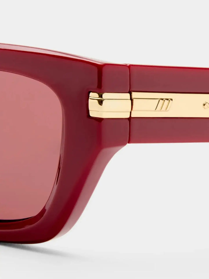 A macro close-up highlighting the polished gold metal hardware inset on the hinge and temple arm of the Le Specs Cubito + | Burgundy sunglasses frame | Twentyseven Toronto