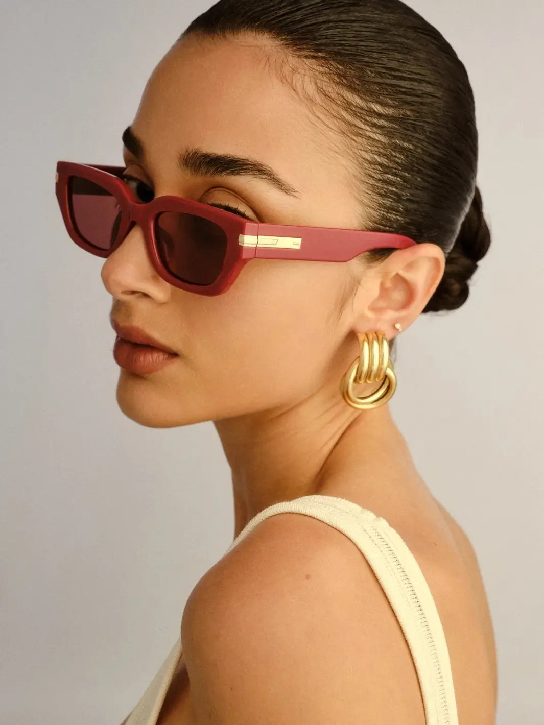 A three-quarter profile view of a woman wearing of the Le Specs Cubito + | Burgundy sunglasses | Twentyseven Toronto
