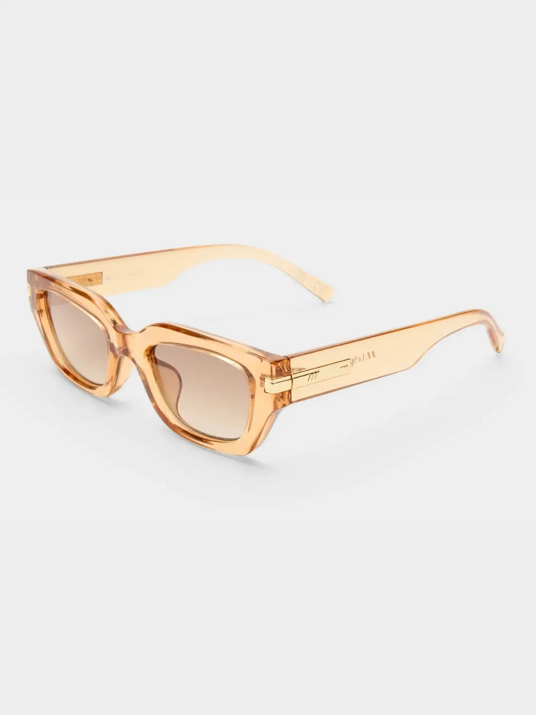 A three-quarter studio product shot of the Le Specs Cubito + | Sand sunglasses showcasing their clear gold frame, brown gradient lenses, and gold-toned temple hardware | Twentyseven Toronto