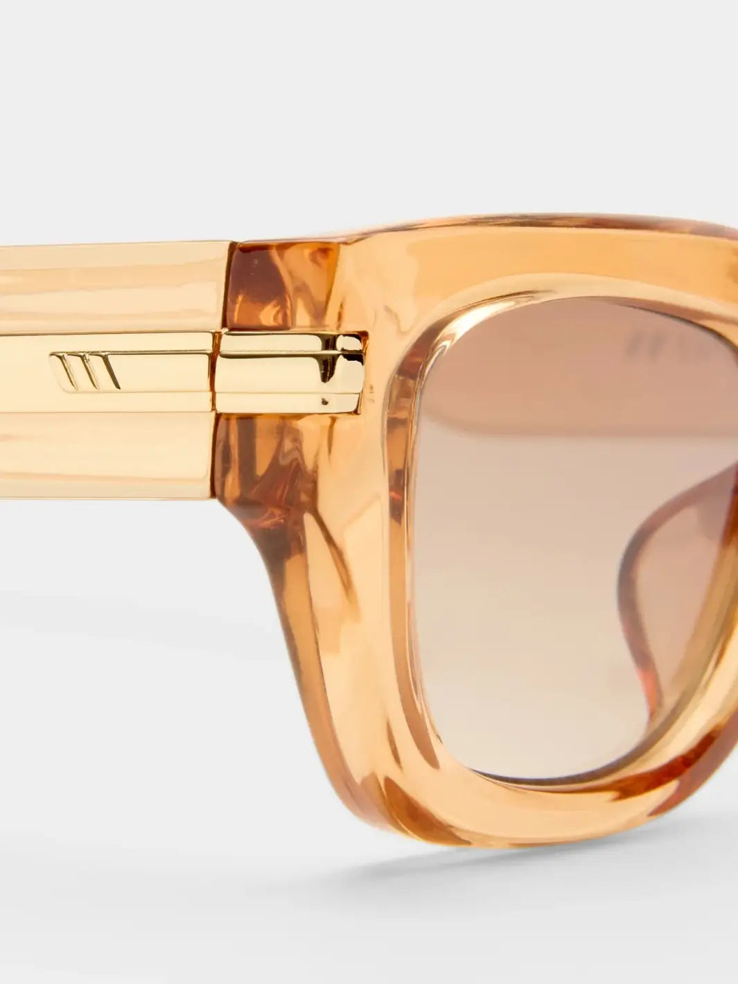 A macro close-up highlighting the sleek gold metal hinge hardware embedded on the side profile of the Le Specs Cubito + | Sand translucent frame | Twentyseevn Toronto