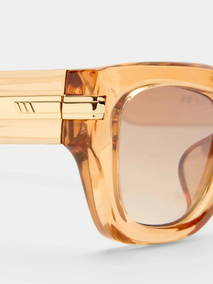 A macro close-up highlighting the sleek gold metal hinge hardware embedded on the side profile of the Le Specs Cubito + | Sand translucent frame | Twentyseevn Toronto