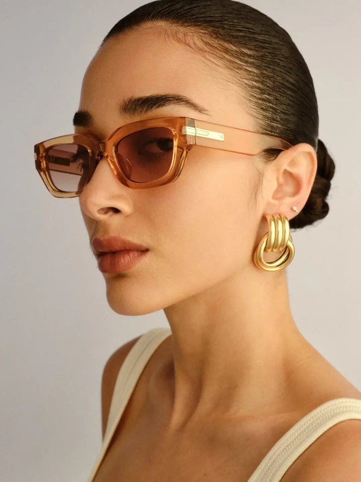 A three-quarter profile studio view of a woman looking over her shoulder wearing  the Le Specs Cubito + | Sand sunglasses | Twentyseven Toronto