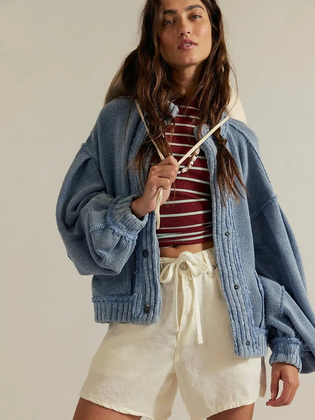 A model poses wearing the oversized, drop-shoulder Free People Cute In This Cardi - Dusty Blue layered over a striped shirt and white shorts | Twentyseven Toronto