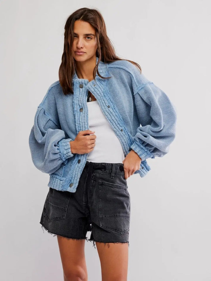 A full-length studio shot features a model wearing the open Free People Cute In This Cardi - Dusty Blue styled with a white tank top and dark grey denim shorts | Twentyseven Toronto