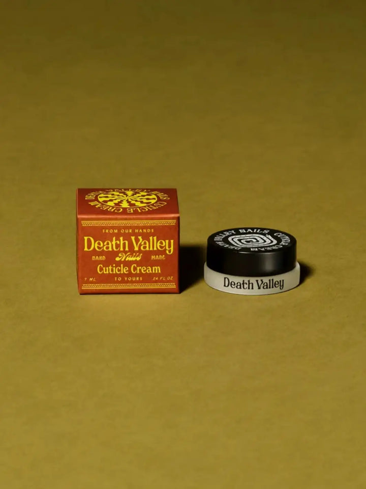 The brown outer packaging and small jar for Death Valley Nails Cuticle Cream - Eucalyptus + Peppermint + Lavender are placed together on a solid green background | Twentyseven Toronto