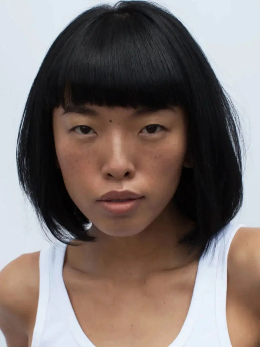 A front-facing headshot of a model with a clean, dark bob and straight bangs styled with R+Co DALLAS Biotin Thickening Shampoo | Twentyseven Toronto