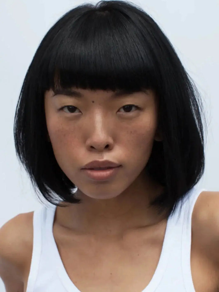 A front-facing headshot of a model with a clean, dark bob and straight bangs styled with R+Co DALLAS Biotin Thickening Shampoo | Twentyseven Toronto