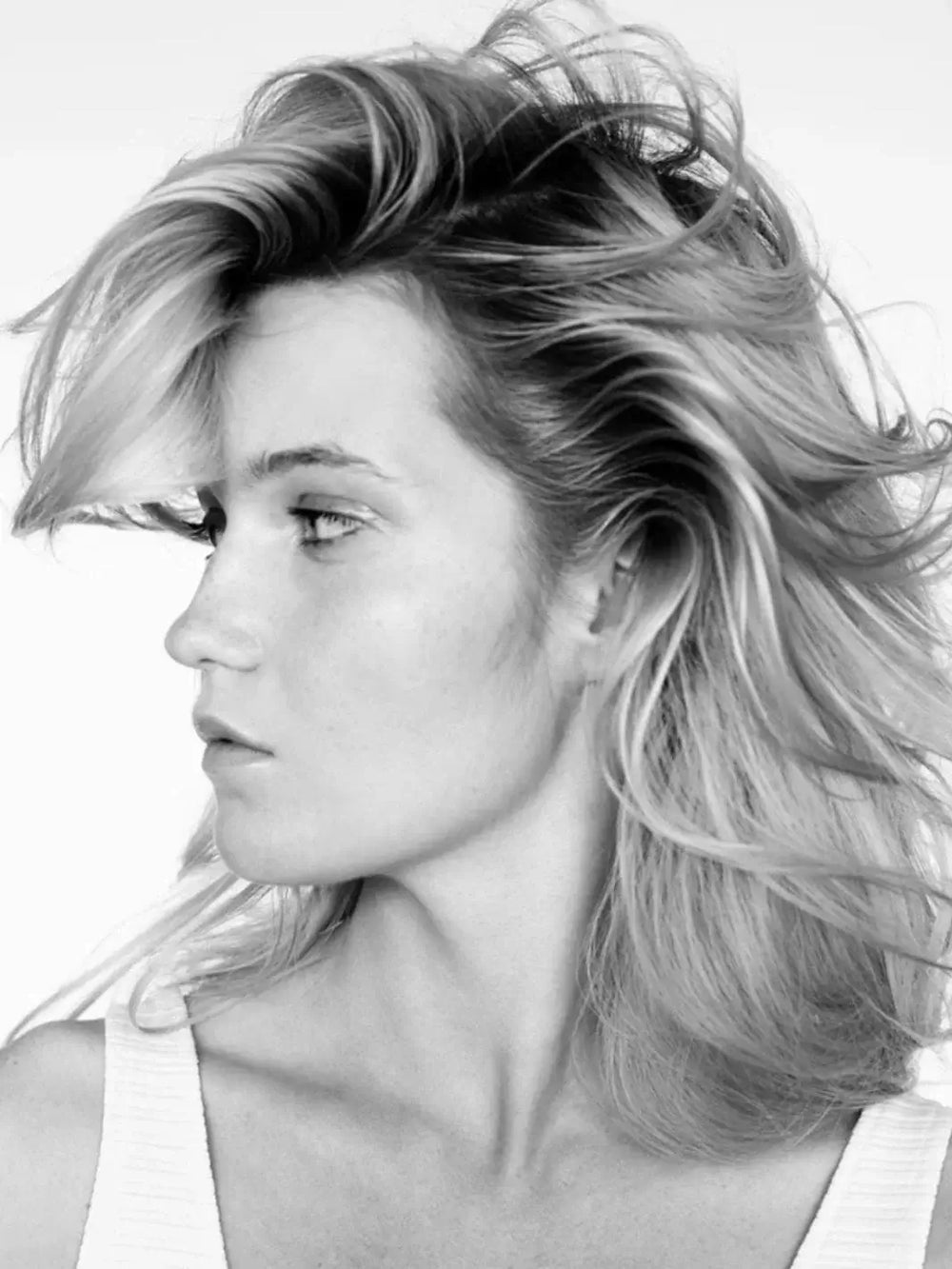 A black and white profile shot of a model showcasing voluminous, windswept hair styled with R+Co DALLAS Thickening Spray | Twentyseven Toronto