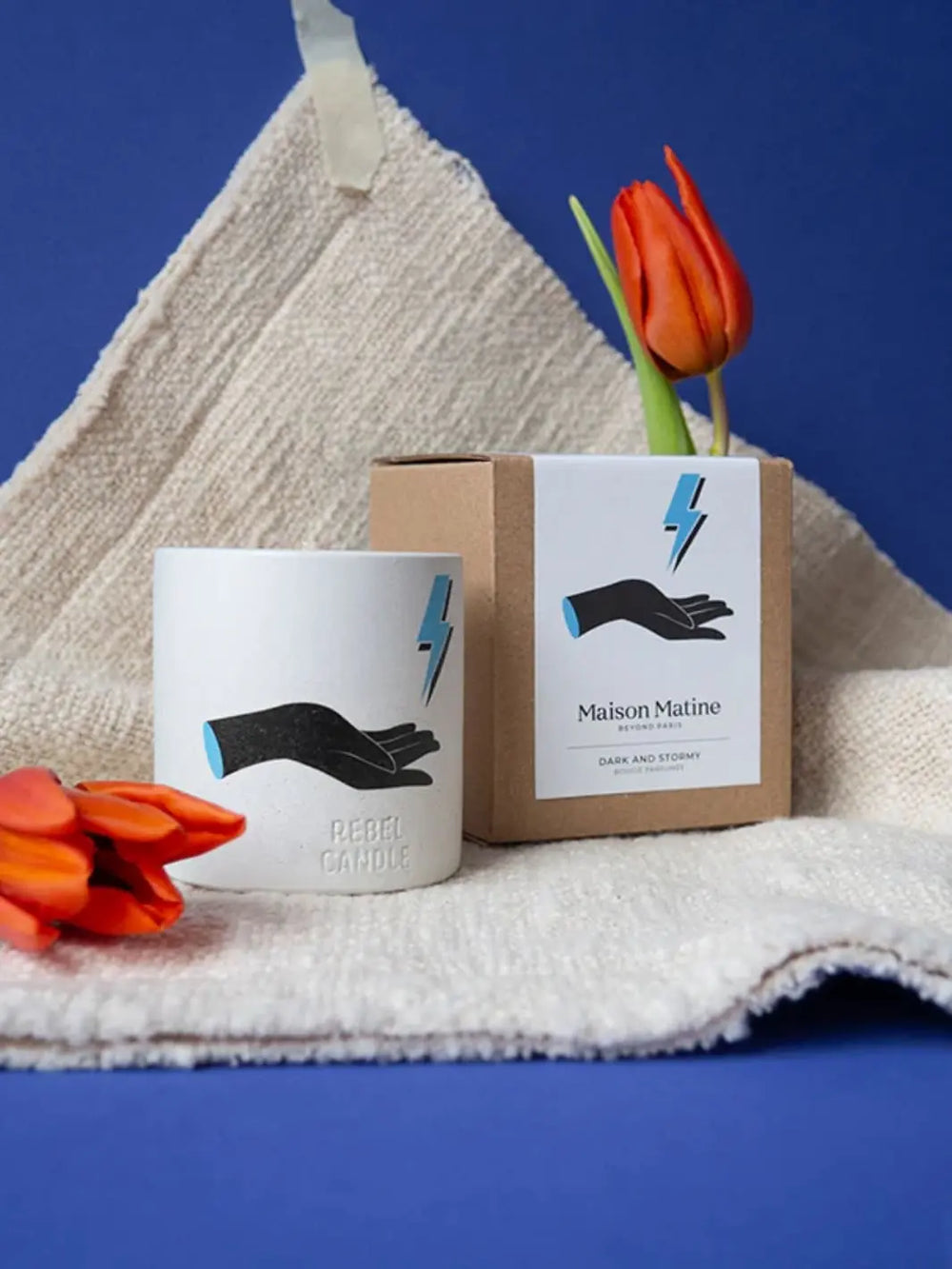 Maison Matine Dark and Stormy Scented Candle with hand design and lightning design with red tulips on a towel against a blue background 160g | Twentyseven Toronto