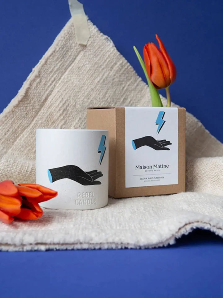 Maison Matine Dark and Stormy Scented Candle with hand design and lightning design with red tulips on a towel against a blue background 160g | Twentyseven Toronto