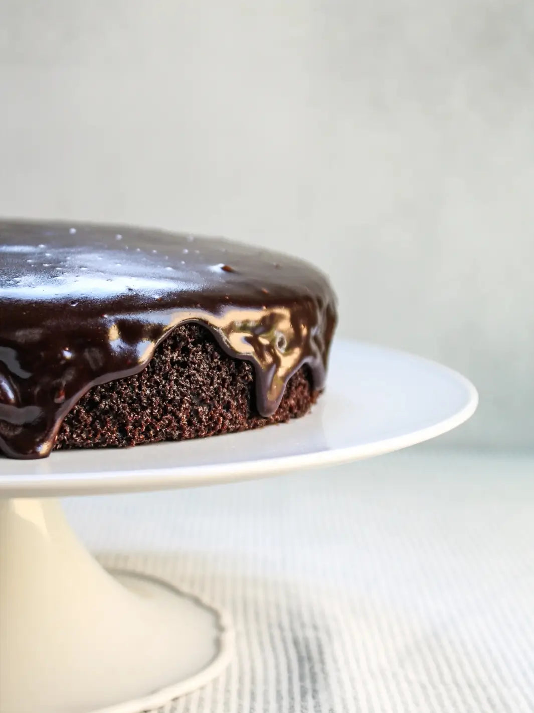 A close-up shot captures thick chocolate glaze dripping down the side of a single-layer chocolate cake prepared from the Glazed Cake Co Dark Chocolate Cake Mix | Twentyseven Toronto