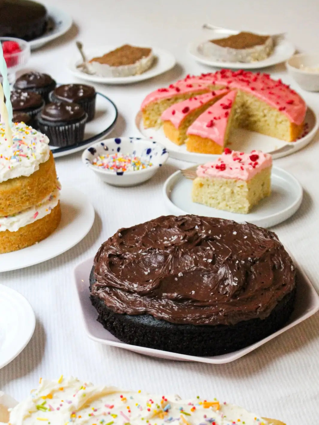 A dessert table display showcases a variety of baked goods, including a finished cake made from the Glazed Cake Co Dark Chocolate Cake Mix topped with swirled frosting and sea salt alongside several cupcakes | Twentyseven Toronto