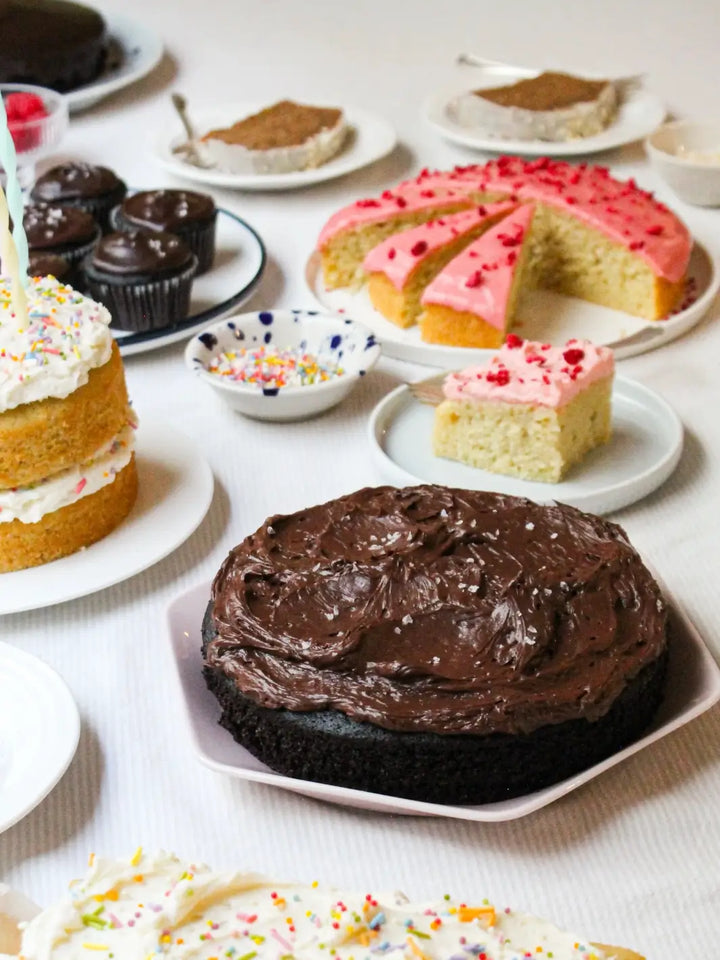 A dessert table display showcases a variety of baked goods, including a finished cake made from the Glazed Cake Co Dark Chocolate Cake Mix topped with swirled frosting and sea salt alongside several cupcakes | Twentyseven Toronto