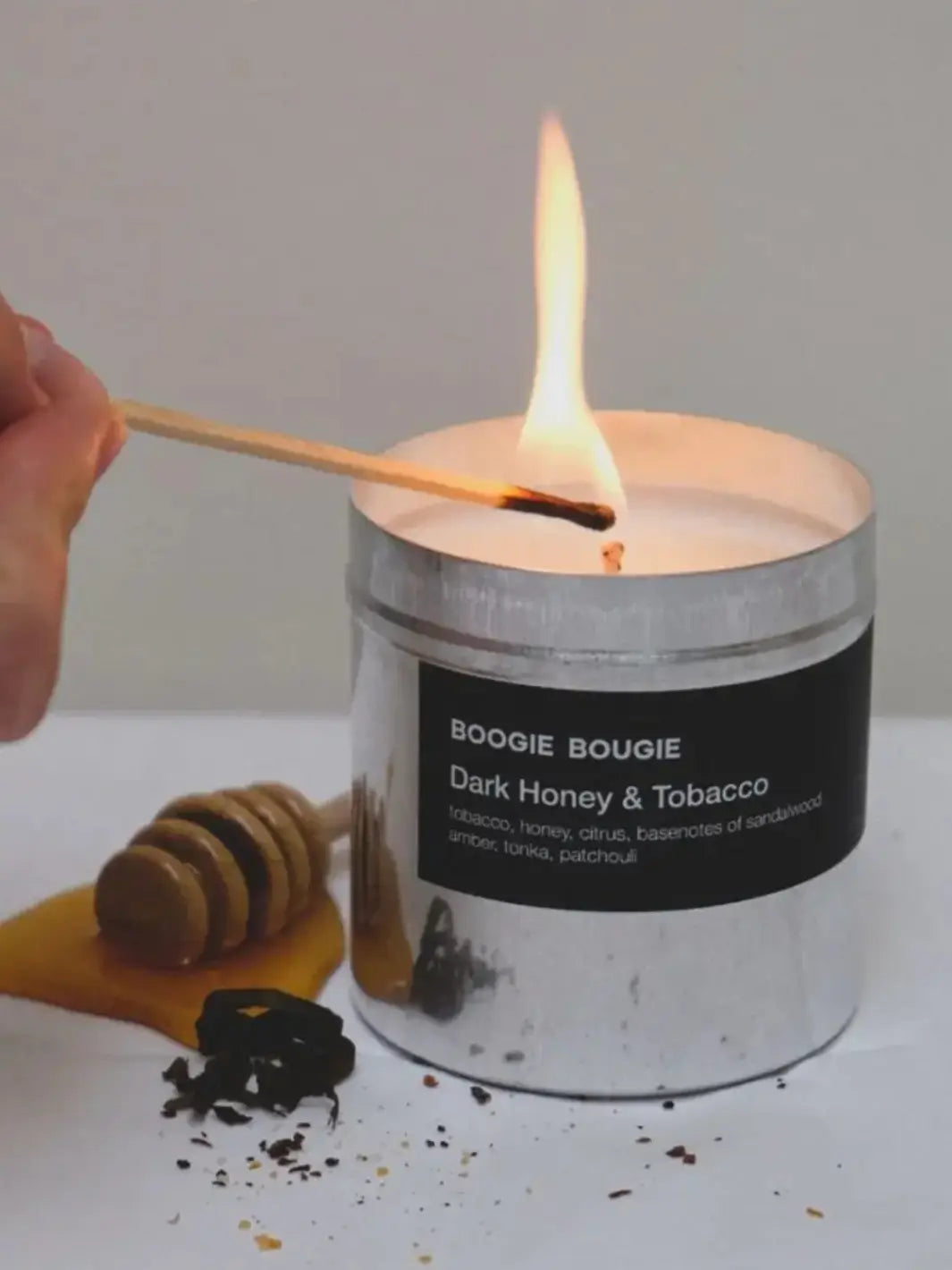 Tin candle labeled 'Boogie Bougie Dark Honey & Tobacco' being lit with a match | Twentyseven Toronto