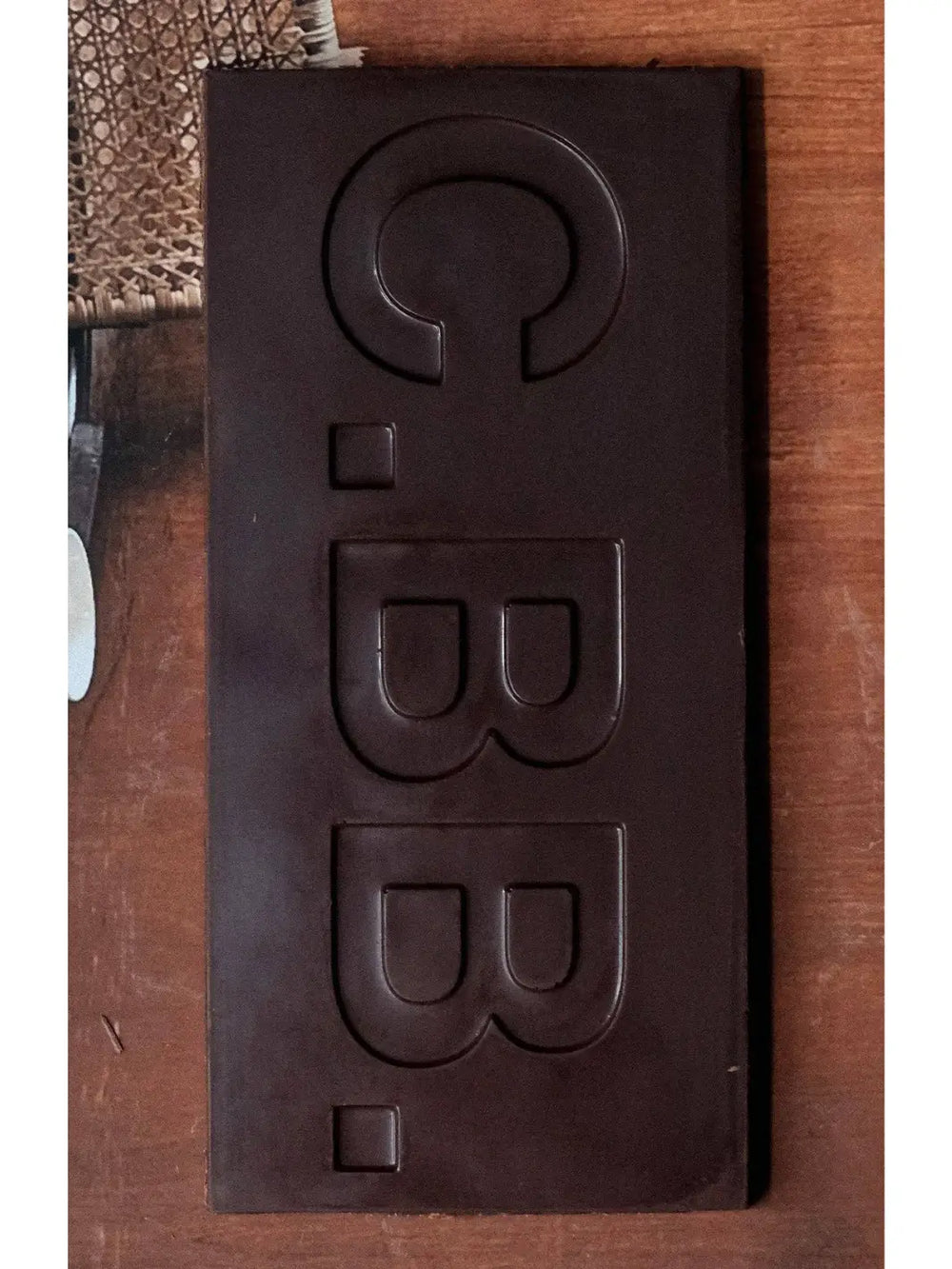 Close-up of the Date Caramel 74% Chocolate Bar from Casa Bosques, showing the smooth dark chocolate surface embossed with the brand's signature "C.B.B." lettering against a wooden background | Twentyseven Toronto
