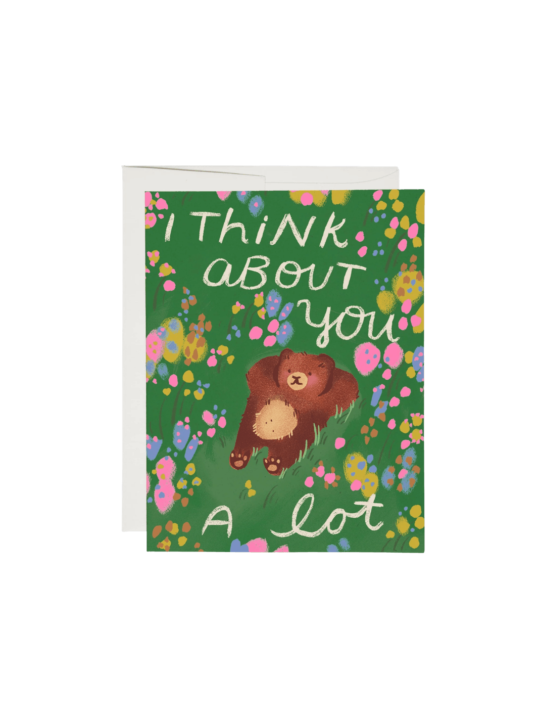 A Daydreaming Greeting Card by Dylan Mierzwinski for Red Cap Cards features an illustration of a brown bear lying on his back in a grassy field of flowers beneath the text "I think about you a lot," next to a white envelope | Twentyseven Toronto