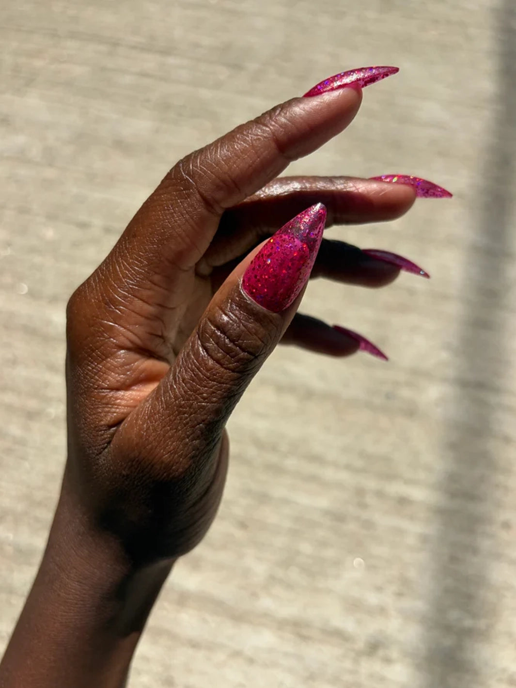 Pink multichrome glitter nail polish on long almond-shaped nails in direct sunlight | Twentyseven Toronto