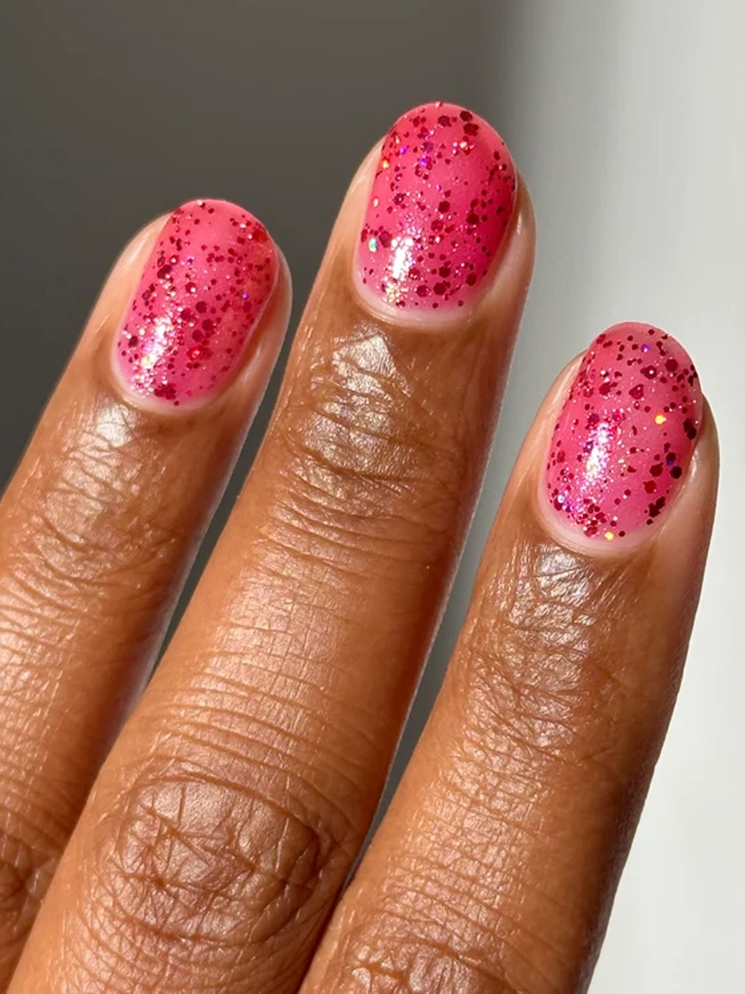 Pink holographic glitter nail polish on short natural nails in sunlight | Twentyseven Toronto