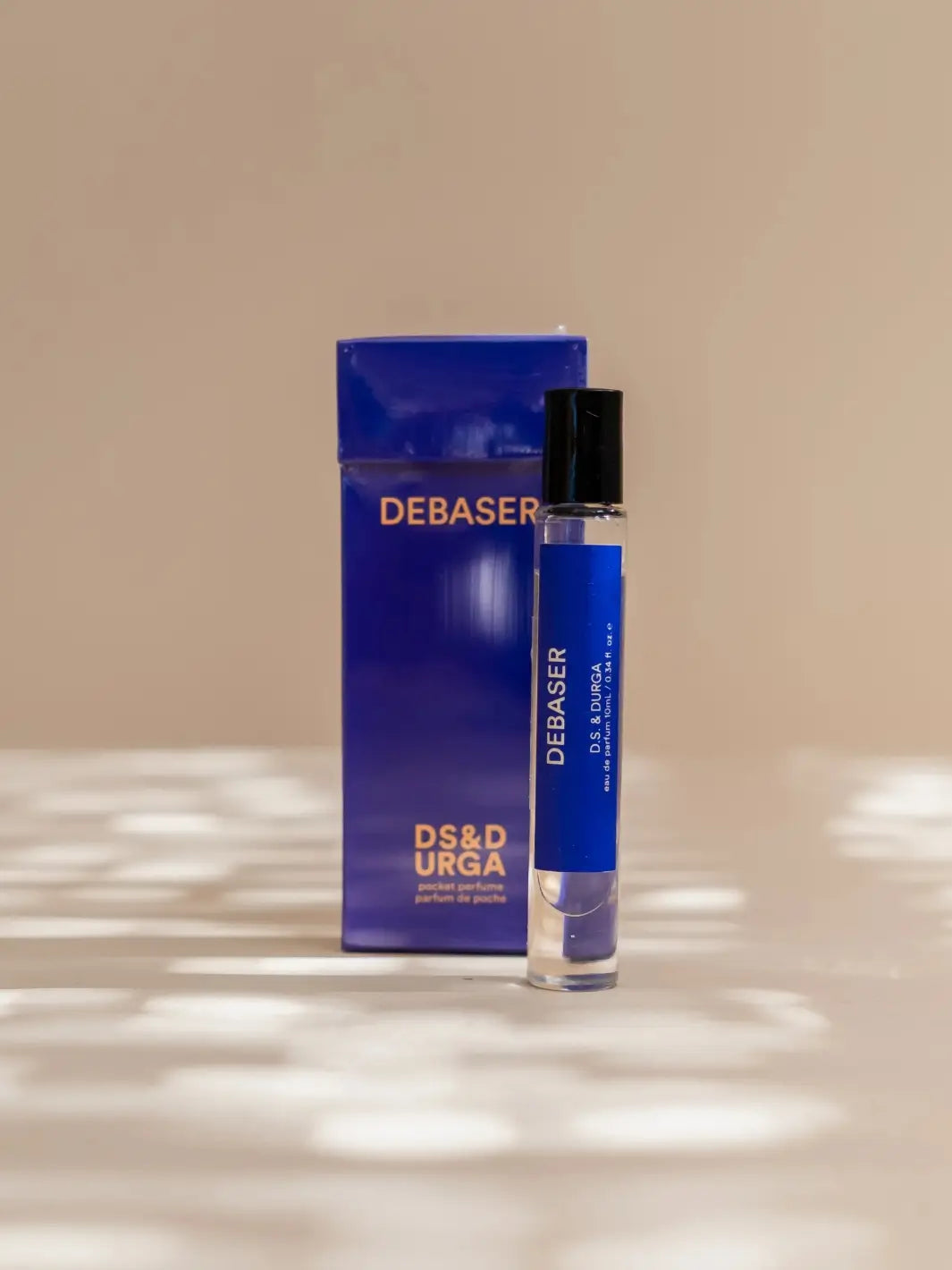 DS&Durga 10ml purple perfume roller bottle and packaging with 'Debaser' branding on a beige surface | Twentyseven Toronto