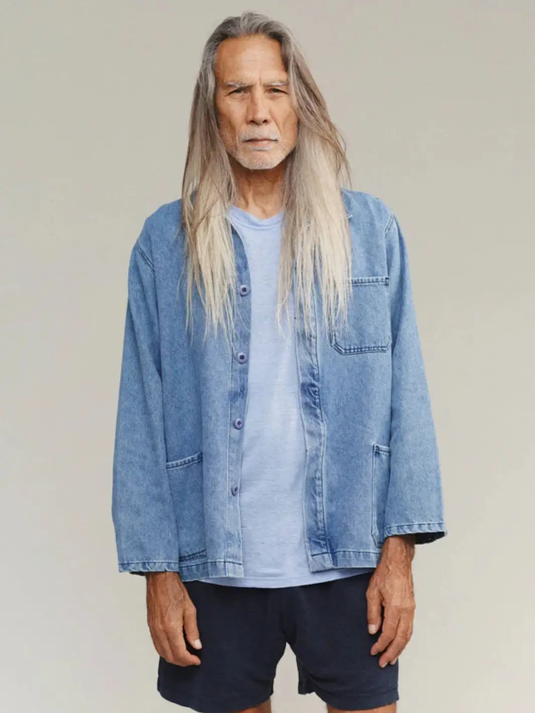 A medium shot captures a model with long hair wearing the relaxed-fit Jungmaven Denim Olympic Jacket in Light layered over a light blue crewneck tee and dark shorts | Twentyseven Toronto